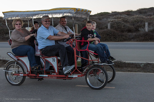 Smiling family of six peddle 4-wheel bike surrey #70 with fringed roof.
