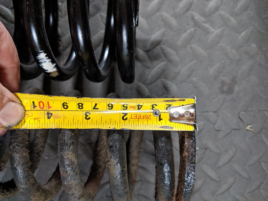 Tape measure showing the 1.5 inch difference in length between the new and old coil springs.